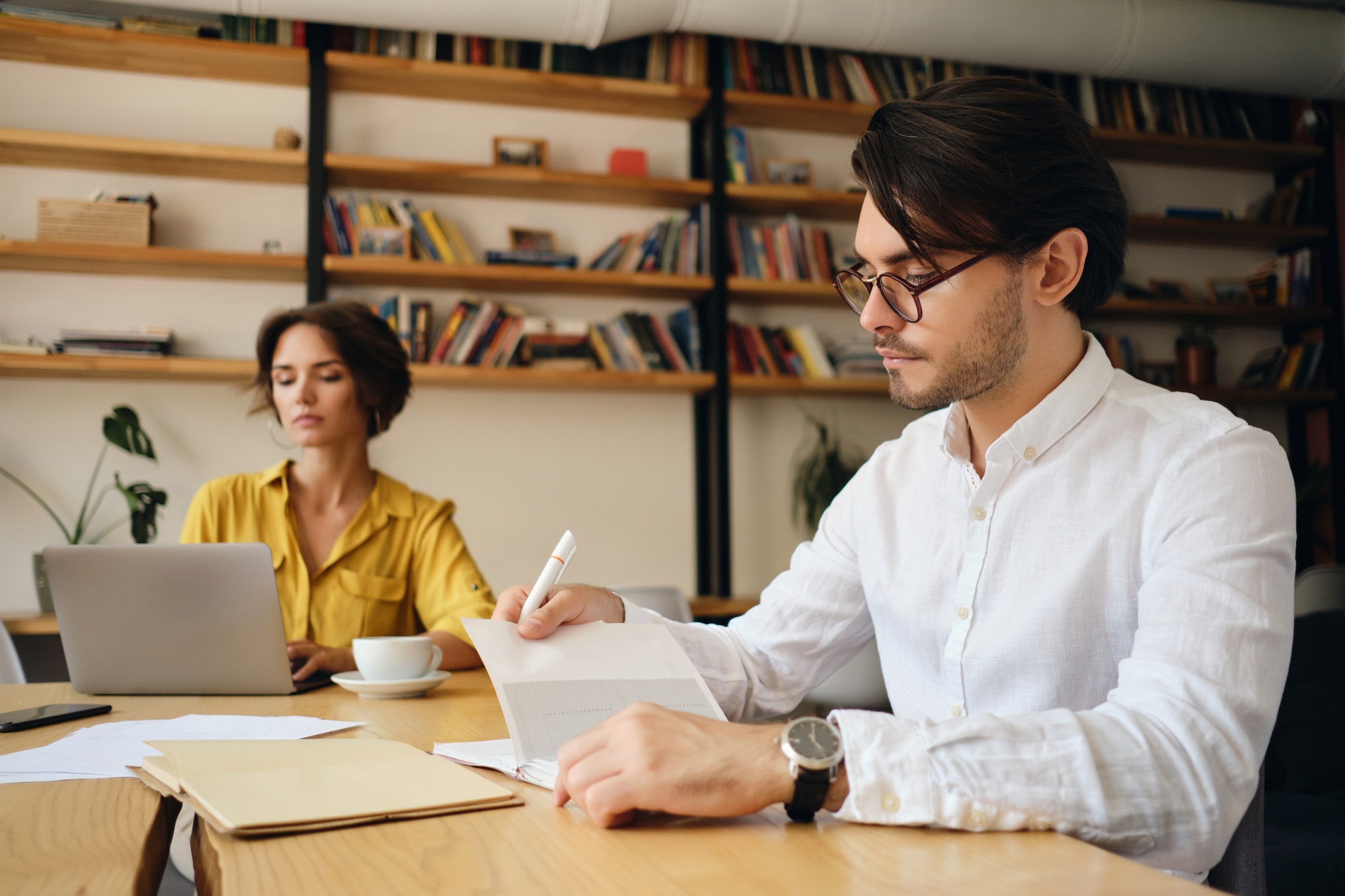 Handsome man in modern office thoughtfully planning work with colleague on background